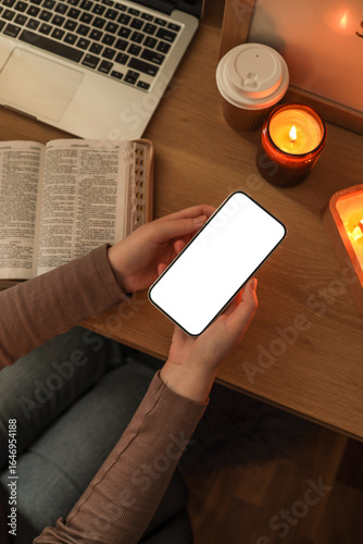 Canvas Print Person holding a smartphone with a blank white screen at a wooden desk, next to