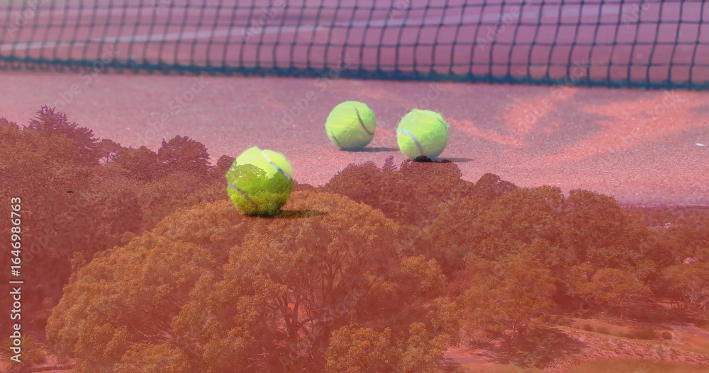 Fototapeta premium Resting three yellow tennis balls on red clay court, with tennis net and forest overlay