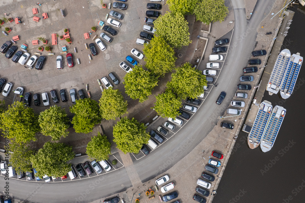 Aerial view of cars neatly parked in designated spots near the waterfront, accentuated by vibrant green trees and boats docked nearby, Gothenburg, Vastra Gotaland, Sweden. Aerial view of cars neatly parked in designated spots near the waterfront, accentuated by vibrant green trees and boats docked nearby, Gothenburg, Vastra Gotaland, Sweden.