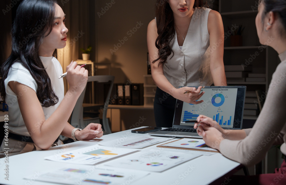 Fototapeta premium Asian businesswomen discussing charts on laptop at night