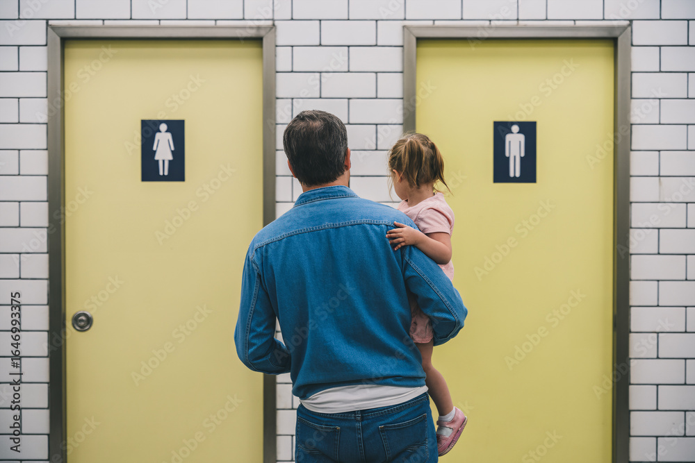 Fototapeta premium Father with young daughter hesitating in front of men’s and women’s restroom doors. Concept of gendered public toilet challenges for parents