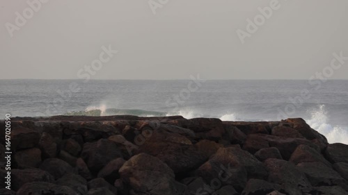 Smooth panoramic movement capturing a wave passing by a surfer and crashing into a stone jetty on a cold winter morning. Beautiful ocean scenery with cinematic atmosphere. Shot in 4K.