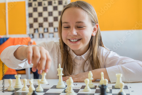 Happy schoolgirl playing chess game in school classroom. Child girl on chess lesson strategy