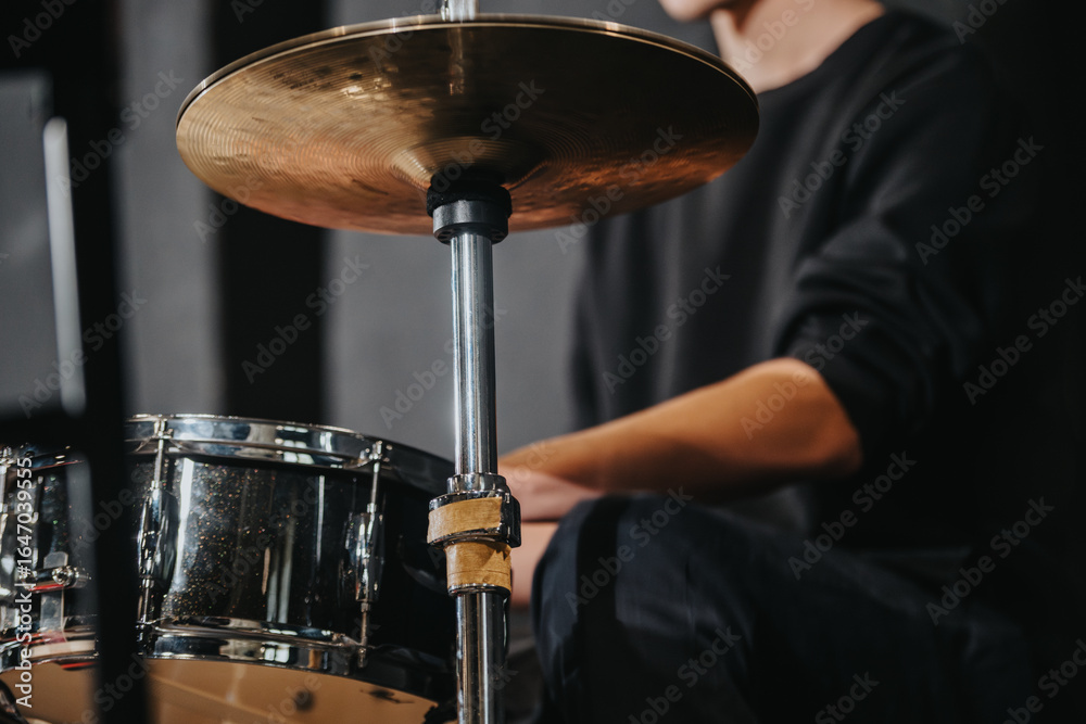 Obraz premium A close-up image of a drummer playing cymbals and snare drum during a lively band rehearsal in a studio environment. The scene highlights musical instruments and the artist's performance posture.