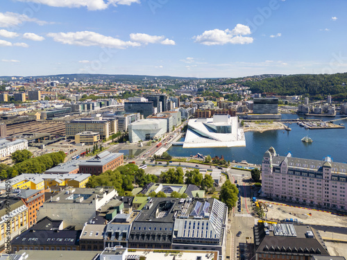 Aerial view of the Oslo Opera House's white marble contrasting against the deep blue fjord, the historic Grand Hotel, and modern city architecture, Oslo, Oslo, Norway.