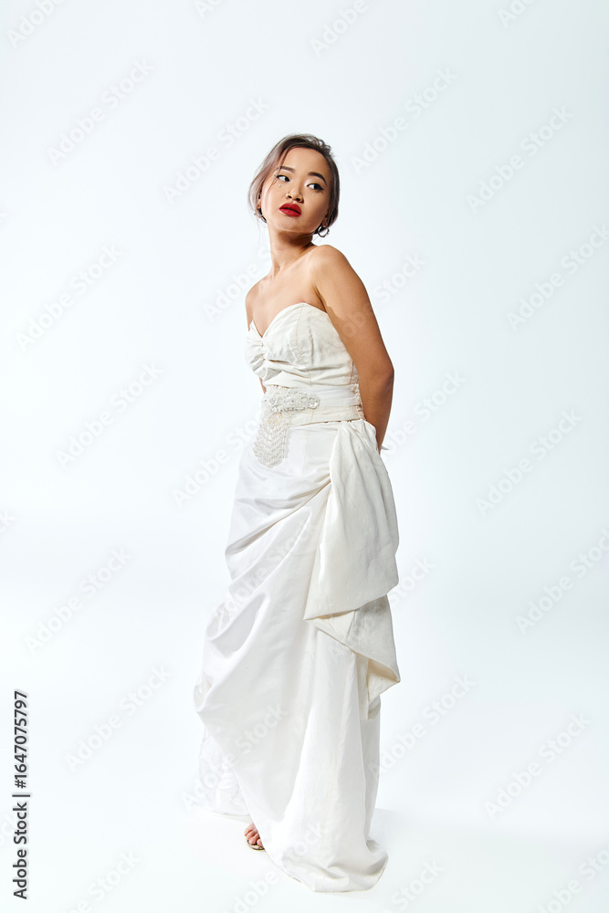Fototapeta premium Elegant young bride in white dress posing gracefully in a serene studio setting