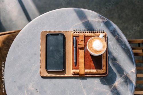 Work Moment with Coffee and Phone: Flat lay of a smartphone, notebook, pen, and a cup of cappuccino on a marble table