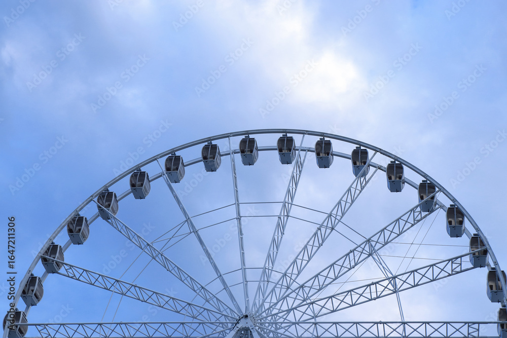 Minimalist view of Ferris wheel silhouette against soft cloudy sky, travel and leisure destination.