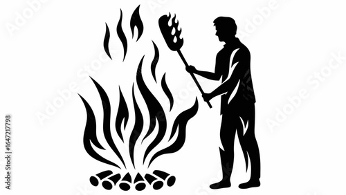 Silhouette of a man tending a large bonfire with flames and logs using a long handled tool outdoors