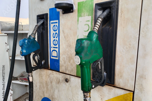 Close-up of diesel and petrol fuel pump nozzles at an Indian gas station, showing blue and green color-coded handles attached to dispenser machine with old paint and visible fuel pipes