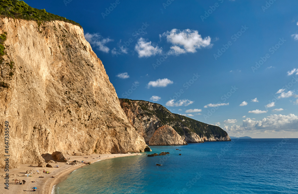 Fototapeta premium People and umbrellas on a sandy beach at the foot of a rocky cliff on the island of Lefkada