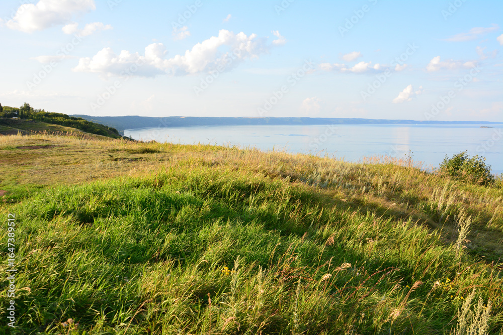 Scenic view of a grassy hillside overlooking a calm body of water in sunset Scenic view of a grassy hillside overlooking a calm body of water in sunset