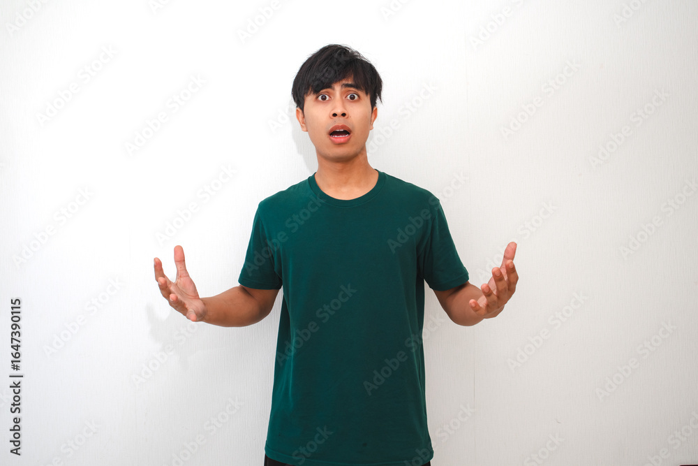 Portrait of a young Asian man standing and looking at the camera with a confused facial expression, isolated on a plain background, perfect for advertisement and emotion concepts Portrait of a young Asian man standing and looking at the camera with a confused facial expression, isolated on a plain background, perfect for advertisement and emotion concepts
