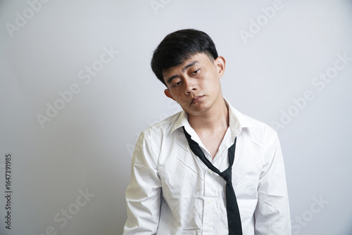 An exhausted young Asian man in a rumpled shirt and tie, looking weary and tired after a long and stressful day at the office.
