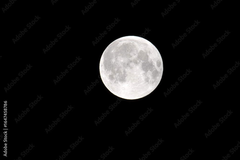 Obraz premium Close-up of a bright full moon against a dark night sky, showing detailed craters and lunar surface textures, captured in high resolution for astronomy and night sky enthusiasts.