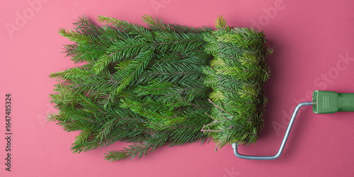 Fotografia Paint roller wrapped in spruce rolls festive green texture on pink background, witty Christmas DIY concept for winter promotions