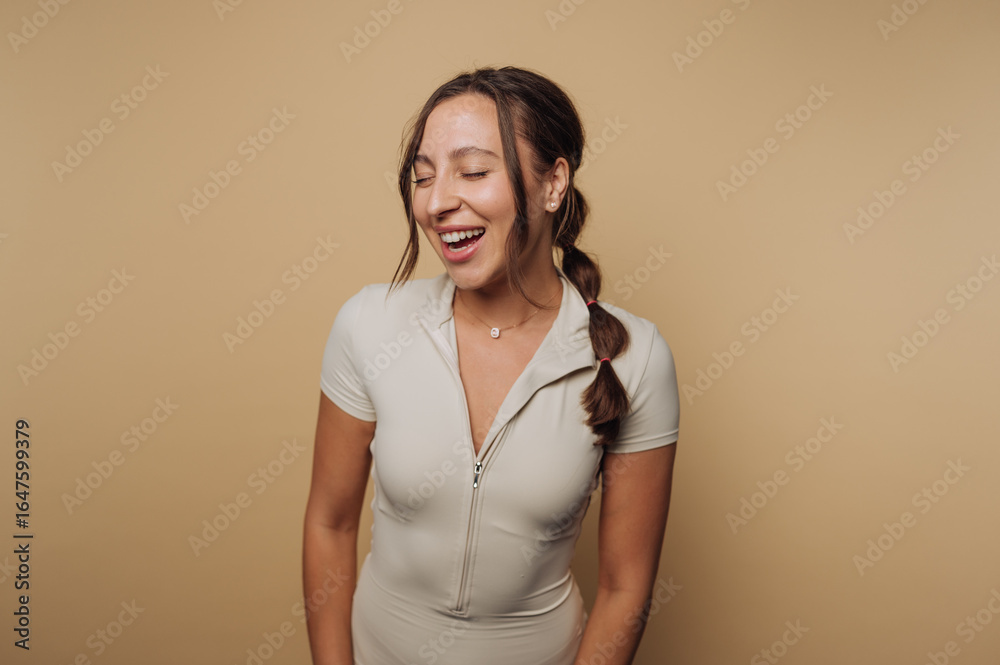 Obraz premium Smiling woman wearing a light-colored outfit in a studio with warm backdrop enjoying a joyful moment