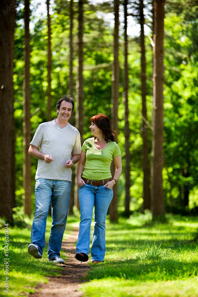 Fototapeta premium A happy mature couple strolling through a leafy forest path smiling and enjoying a sunny summer's day outdoors. From a series of images.