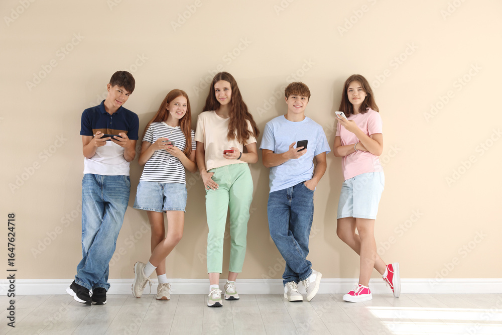 Obraz premium Teenage friends with smartphones near beige wall indoors