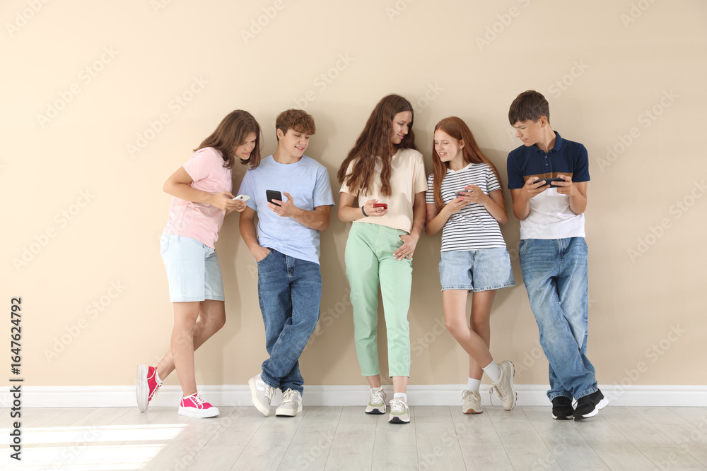 Obraz premium Teenage friends with smartphones near beige wall indoors