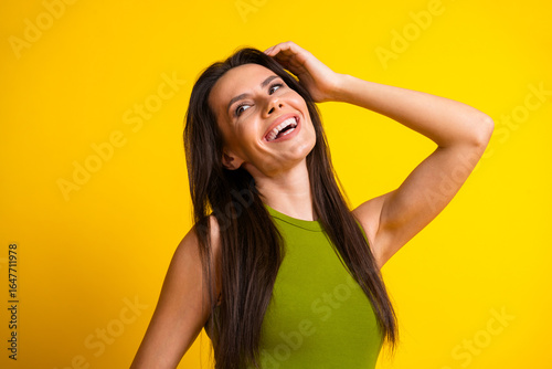 Smiling young brunette woman in green top posing against vibrant yellow background showcasing a joyful and cheerful lifestyle.