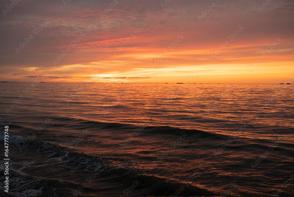 Obraz premium Asnelles-Sur-Mer, France - 08 08 2025: Panoramic view of the sea, waves, artificial port and the colorful cloudy sky at sunset along the jetty