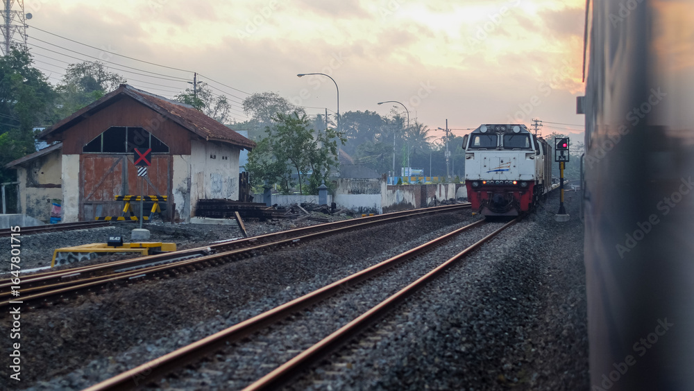 Naklejka premium Indonesian Train Passing Through Railway Tracks at Sunset in a Small Town