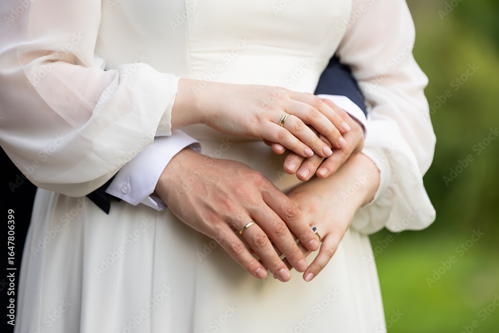 Fototapeta premium Groom embracing bride – close-up of hands and wedding rings