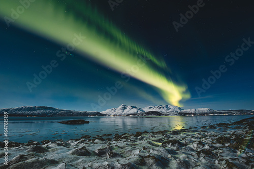 Fotografie Aurora Borealis glows above Norway Malangen Fjord in Troms, painting the starry night with green light