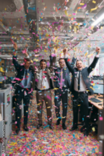 Blurred background of people in business suits celebrating in an office, throwing confetti and holding party streamers. Concept of corporate celebration, team success, and joyful workplace moments.