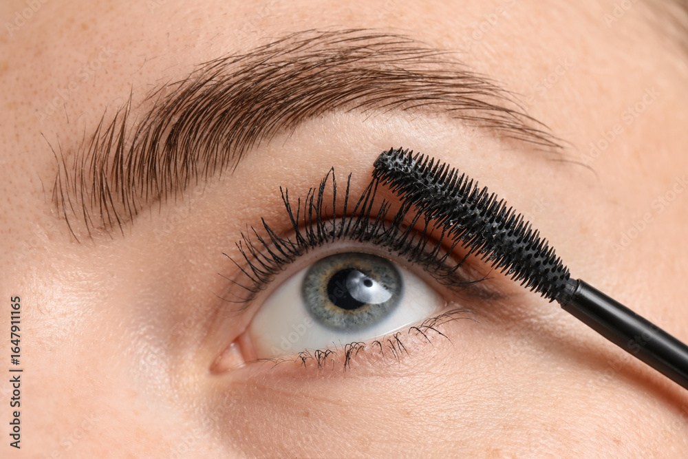 Naklejka premium Young woman applying mascara onto her eyelashes, closeup