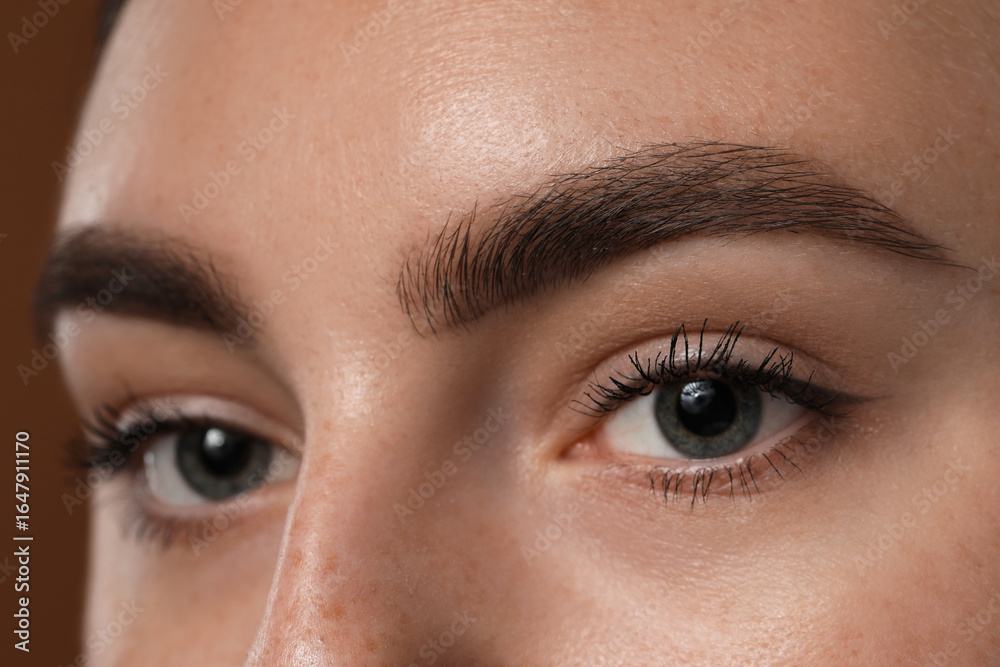Fototapeta premium Young woman with beautiful eyebrows on brown background, closeup