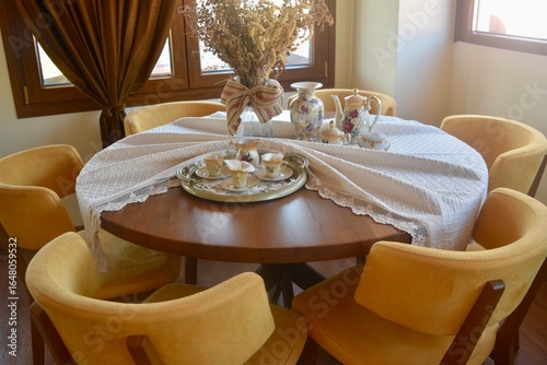 Dining table and chairs in elevated high end restaurant at a grape and olive farm in Crete Greece; decorated with white fabric linen, china plates and tea glasses, and faux dried flowers