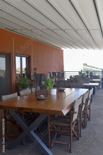 Outdoor patio wooden dining table and chairs on a balcony in Crete Greece; minimally decorated with candle lanterns and greenery plants
