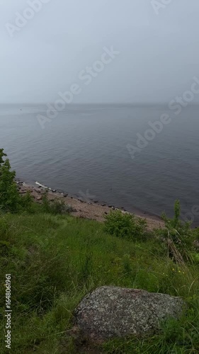 view from green hill to shore with grey sky and lake