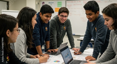 Students collaborate around a table with laptops and charts