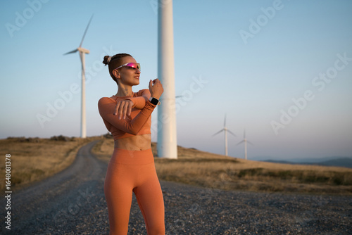 Sportswoman stretching near wind turbines at sunset
