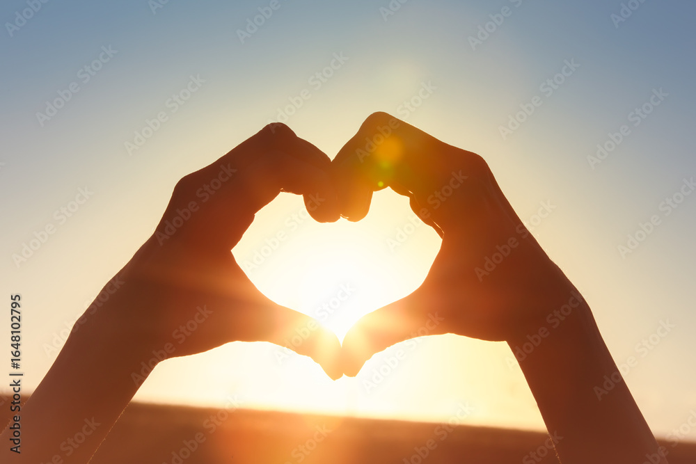 Fototapeta premium Hand making heart shape on beautiful sunset background. 