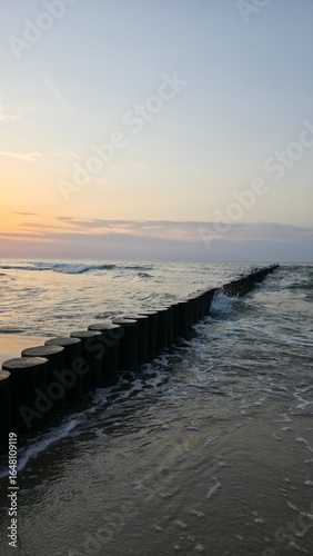 sunset on the beach Wooden breakwater stretching into the sea at sunset, with gentle waves and warm golden light.