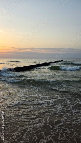 Wooden breakwater stretching into the sea at sunset, with gentle waves and warm golden light.sunset on the beach