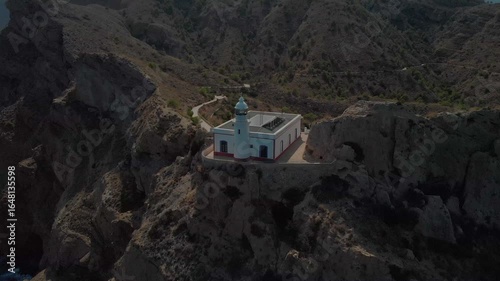 Aerial view of white and red lighthouse on coastal cliff in Spain