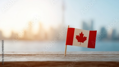 Small Canadian flag stands proudly on wooden surface, symbolizing national pride against blurred city skyline