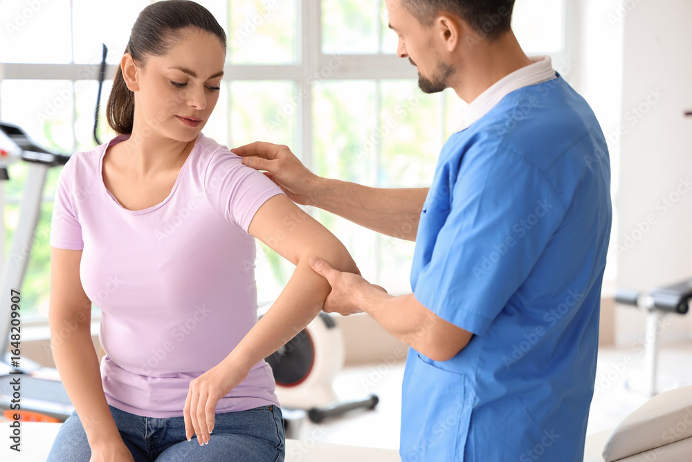 Fototapeta premium Male physiotherapist working with young woman in rehabilitation center