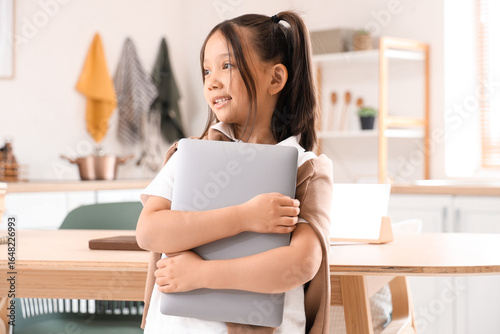 Little Asian girl with laptop in kitchen