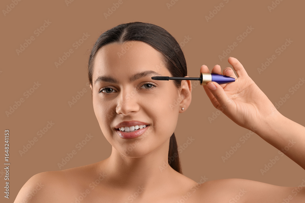 Fototapeta premium Pretty young woman applying mascara on beige background