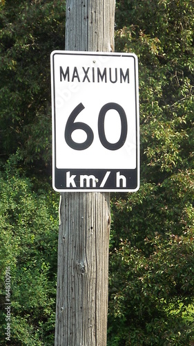 A white speed limit sign mounted on a wooden post. The sign indicates a maximum speed of 60 km per hour.
