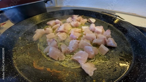 A close-up video of raw chicken cubes being dropped into a hot frying pan over fire for cooking a meal. Close-up chicken cooking in frying pan.