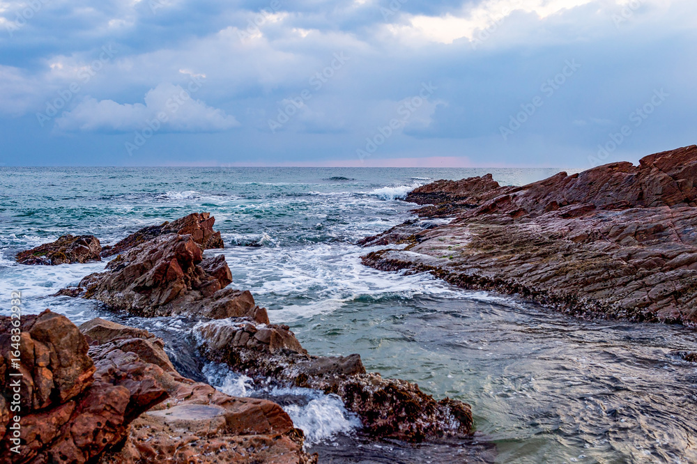 Obraz premium Rocky Coastline with Waves under Dramatic Cloudy Sky