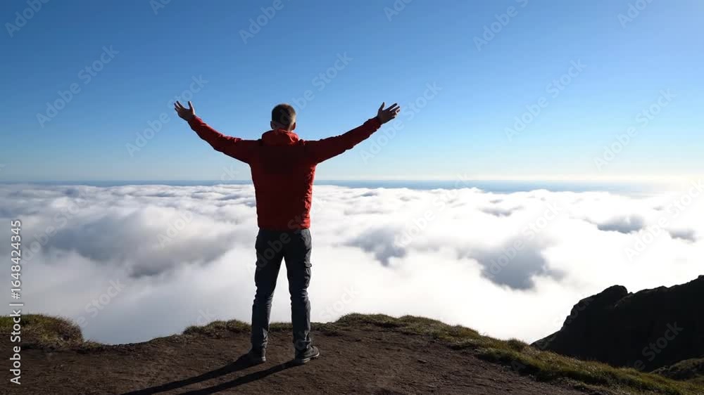 A man stands on a hilltop with arms outstretched, overlooking a sea of clouds under a bright blue sky. A man stands on a hilltop with arms outstretched, overlooking a sea of clouds under a bright blue sky.