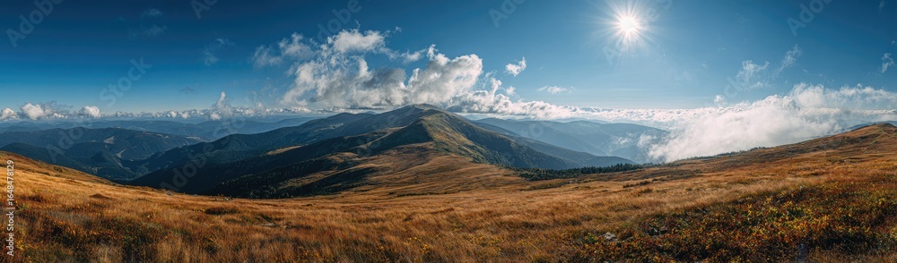 Obraz premium Panoramic view of mountain peaks and valleys under a vibrant sky. Golden-toned meadows stretch across the foreground, leading to rugged,